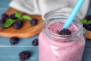 Delicious blackberry smoothie in mason jar on blue wooden table, closeup. Space for text
