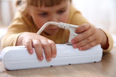 Photo of Little child playing with power strip and plug on floor indoors, selective focus. Dangerous situation
