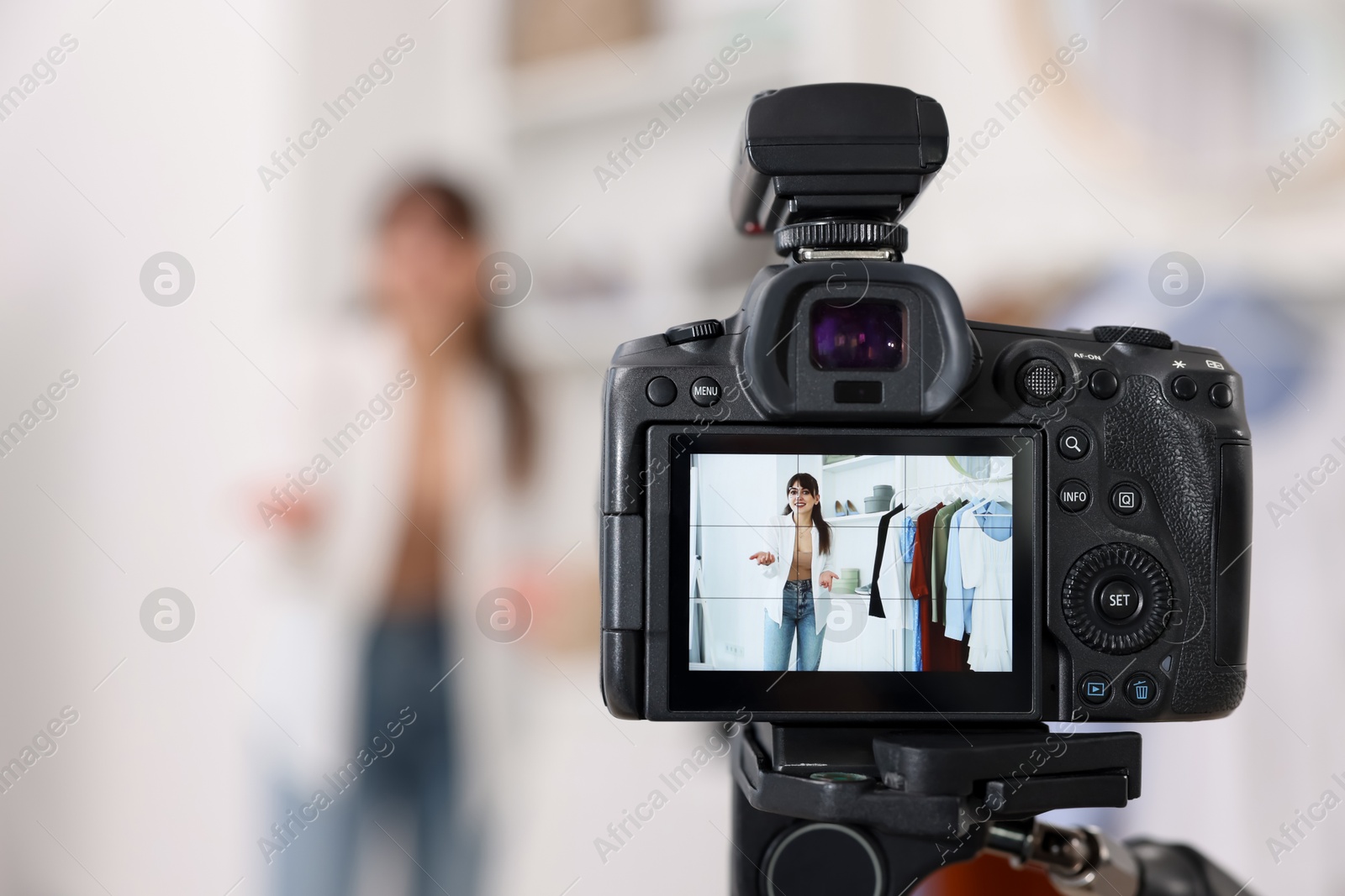 Photo of Fashion blogger showing her clothes while recording video at home, focus on camera