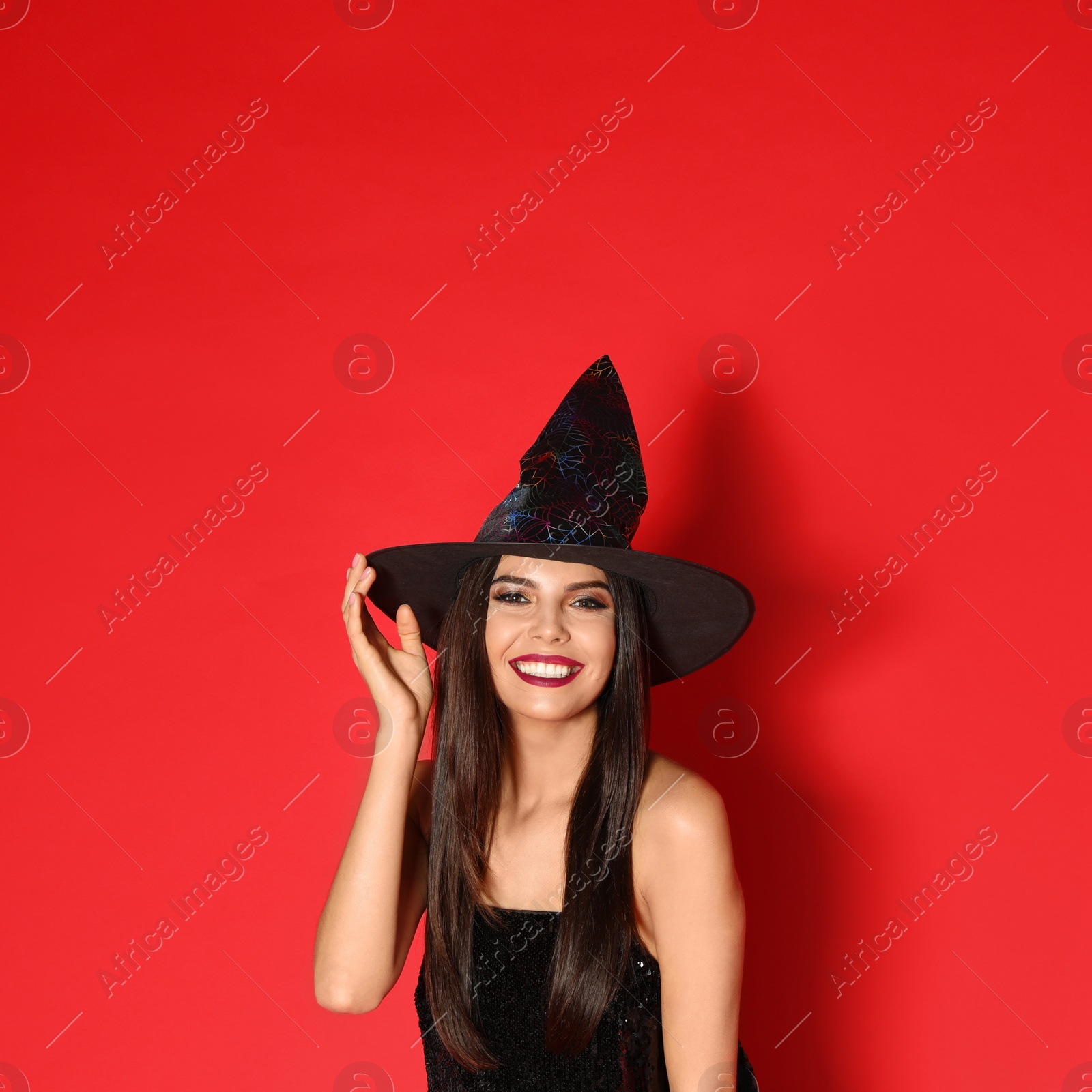 Photo of Beautiful young woman wearing witch costume for Halloween party on red background, space for text