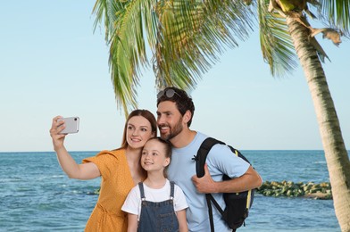 Happy family with child taking selfie near palm on beach