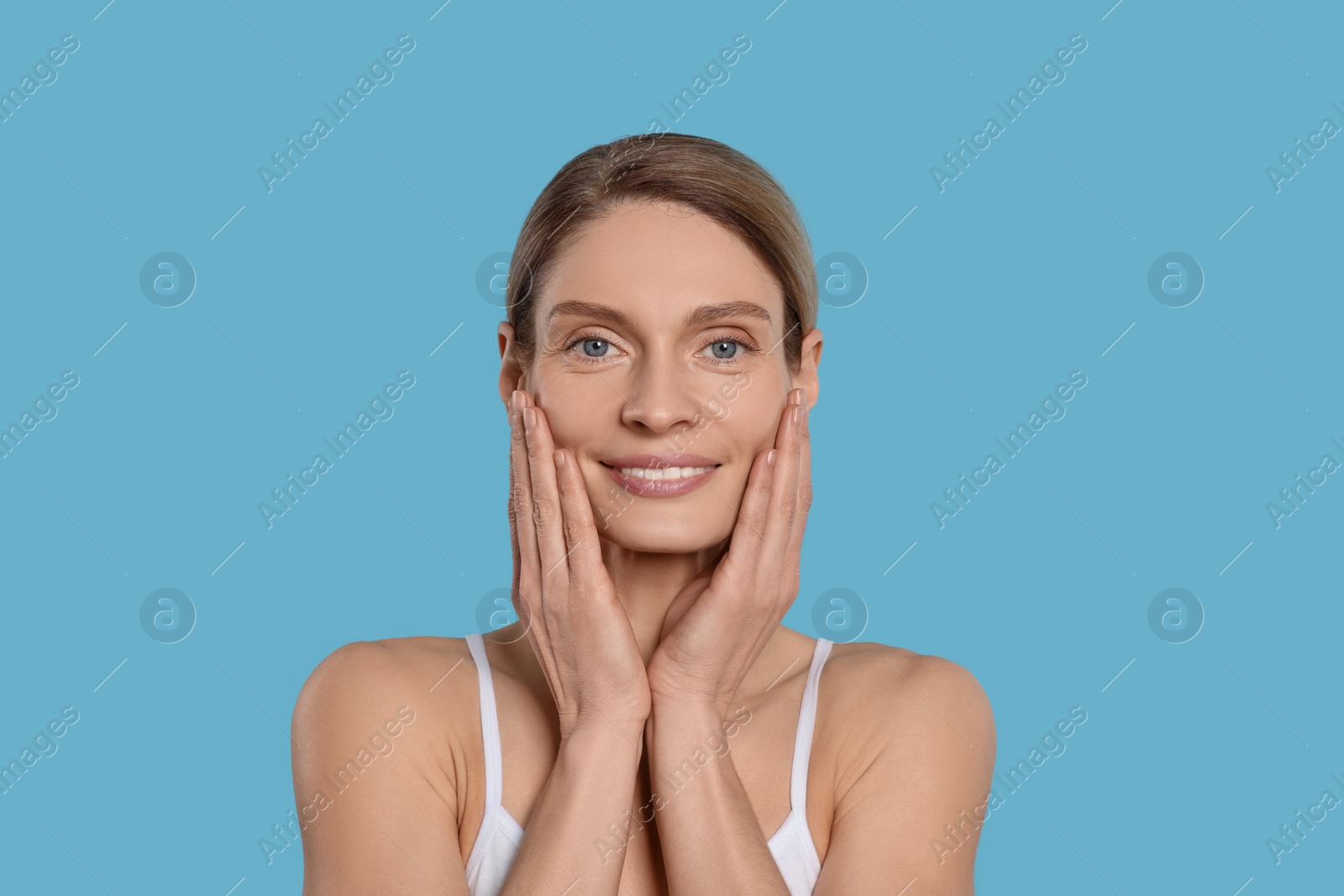 Photo of Woman massaging her face on turquoise background