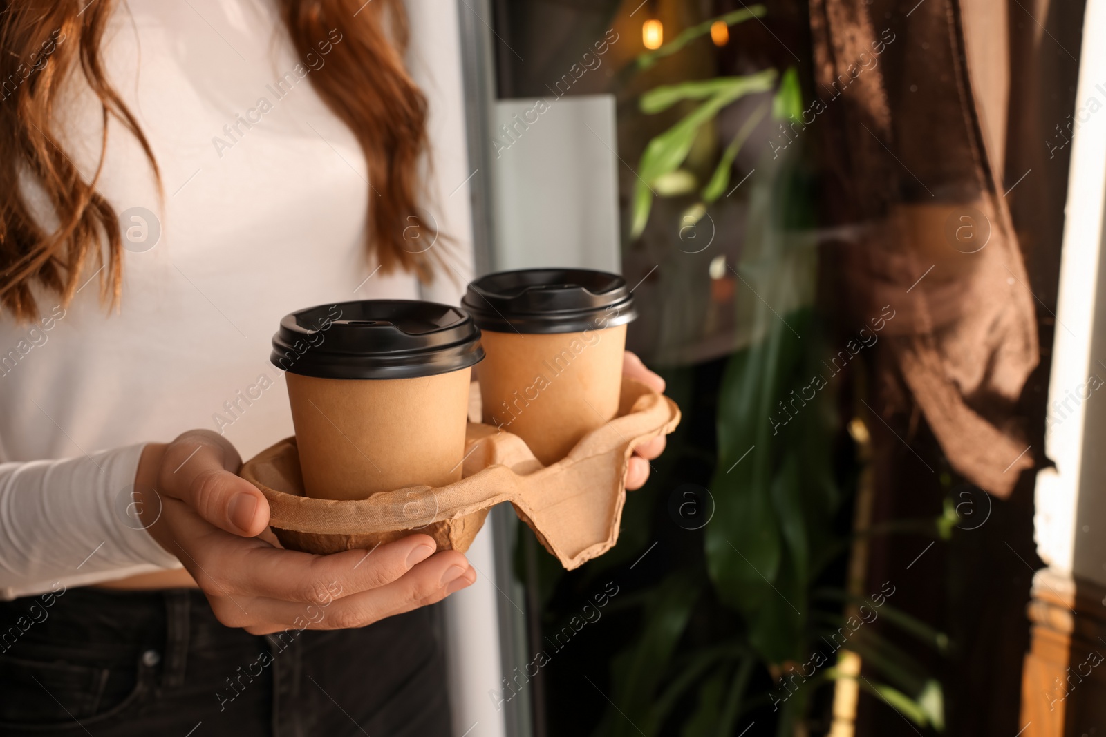 Photo of Woman holding paper coffee cups indoors, closeup. Space for text