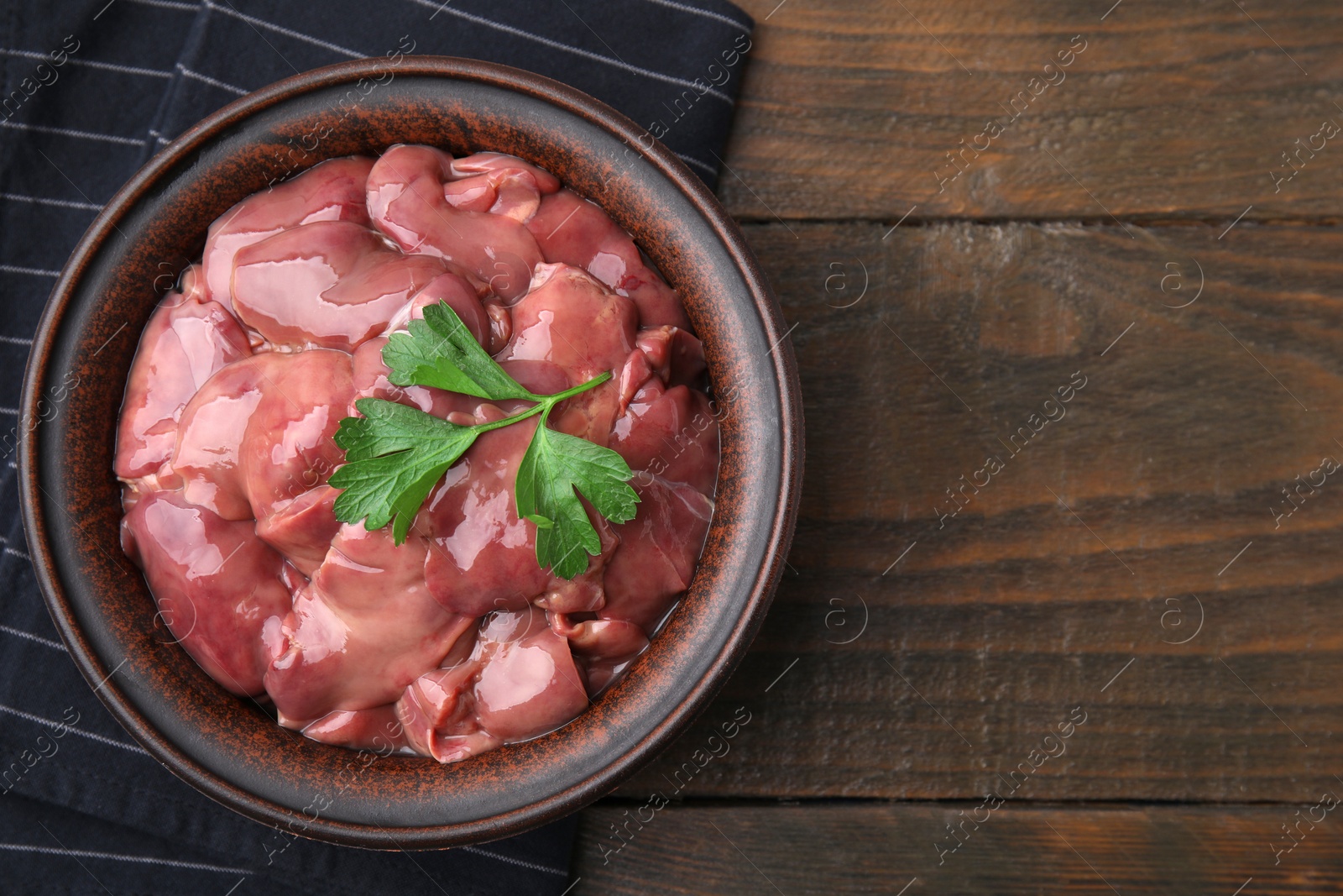 Photo of Bowl with raw chicken liver and parsley on wooden table, top view. Space for text