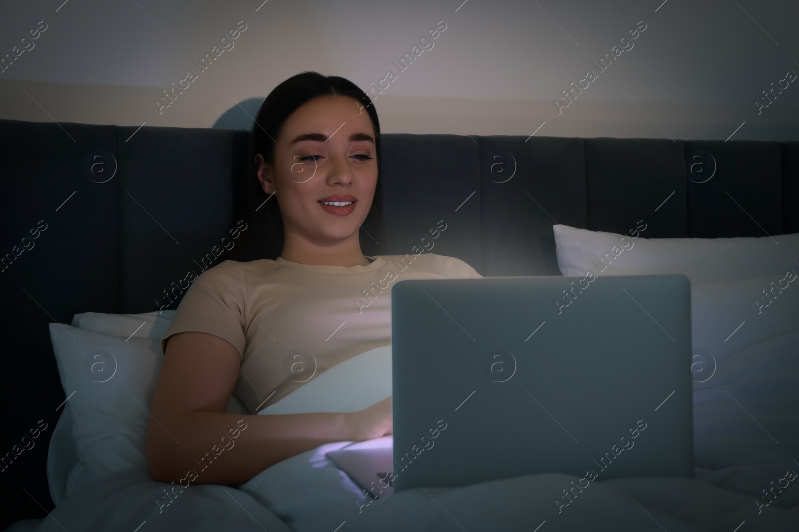 Photo of Young woman using laptop in bed at night. Internet addiction