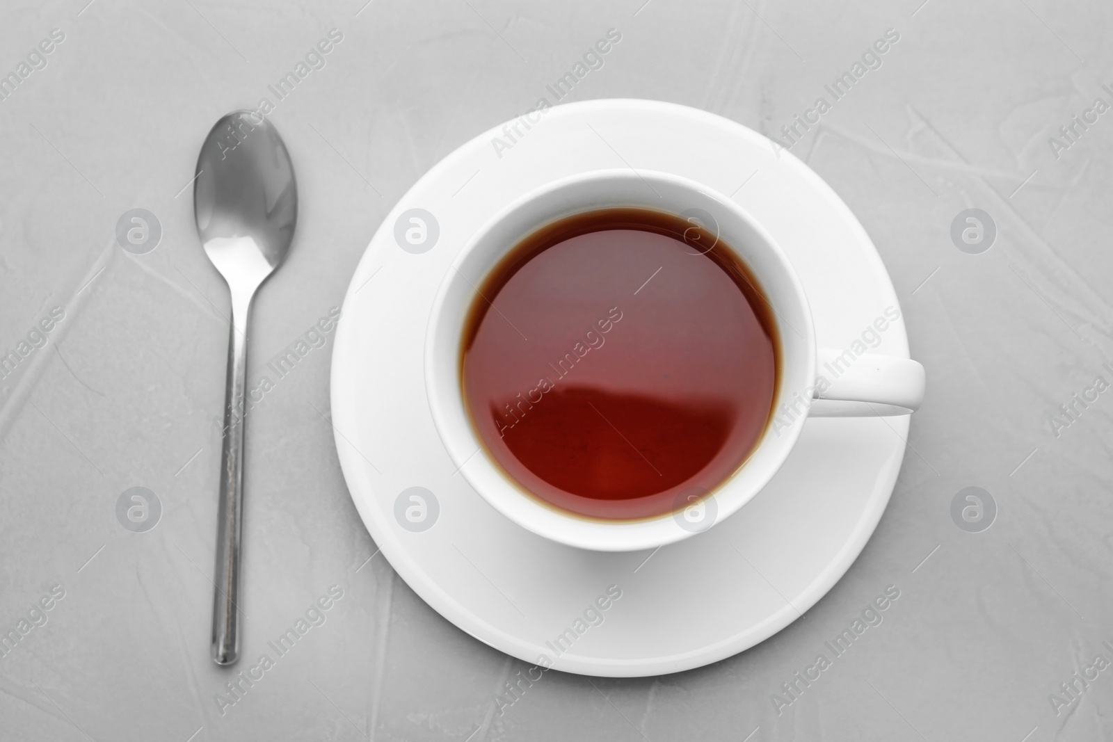 Photo of Cup of tea with saucer and spoon on grey background, flat lay