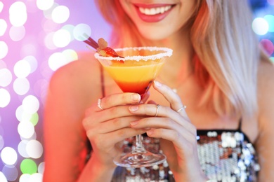 Photo of Young woman with glass of martini cocktail against festive lights, closeup
