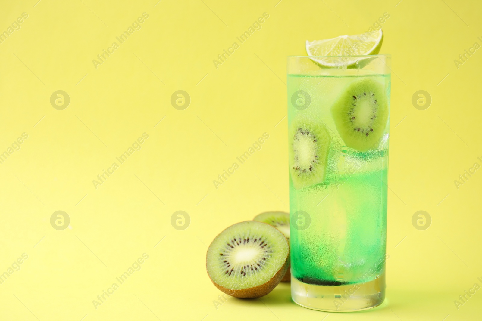 Photo of Glass of refreshing drink and cut kiwi on yellow background, space for text