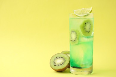 Photo of Glass of refreshing drink and cut kiwi on yellow background, space for text