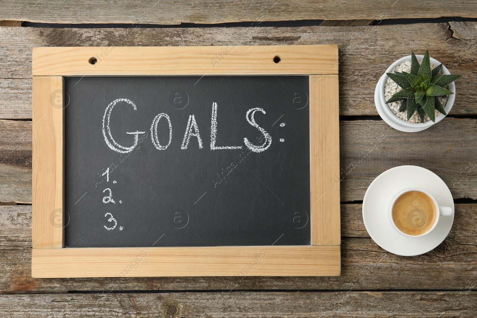 Photo of Small blackboard with empty list of goals, houseplant and cup of coffee on wooden table, flat lay. Space for text