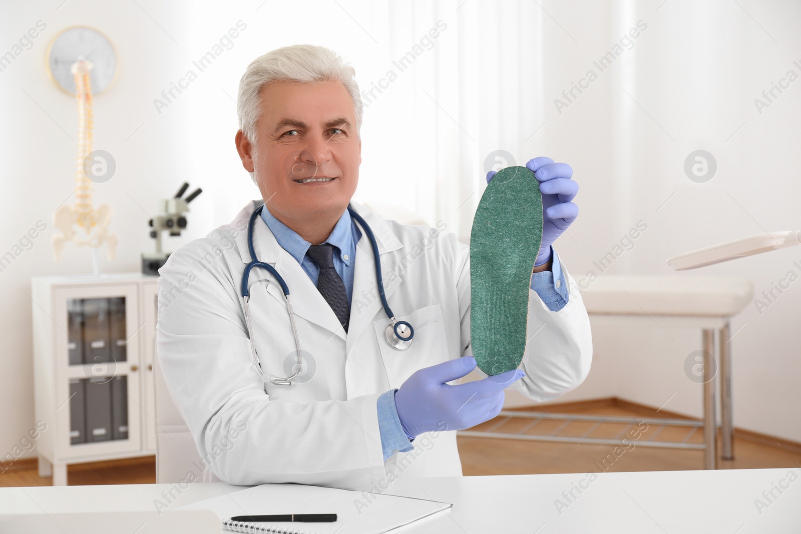 Photo of Senior male orthopedist showing insole in clinic