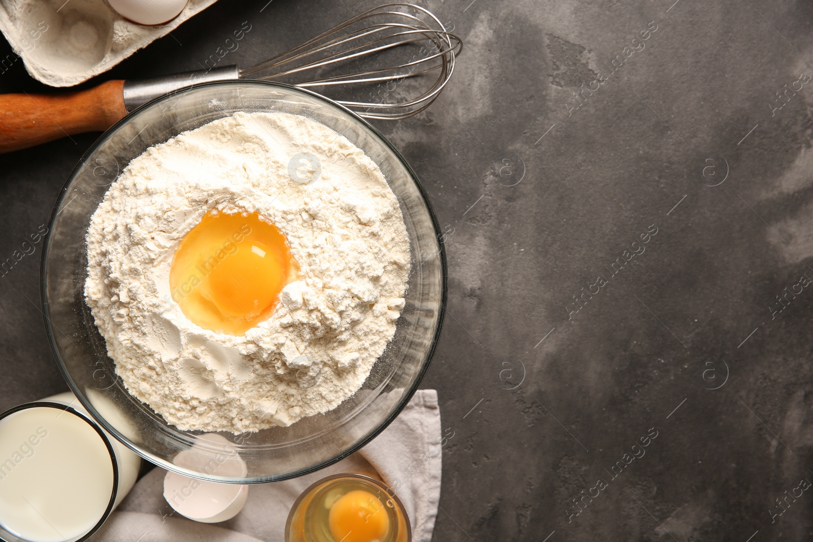 Photo of Making dough. Flour with egg yolk in bowl and other products on grey textured table, flat lay. Space for text