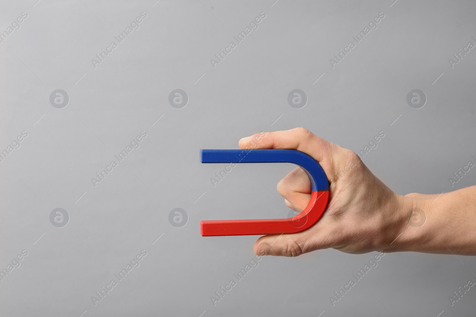 Photo of Man holding magnet on grey background, closeup. Space for text