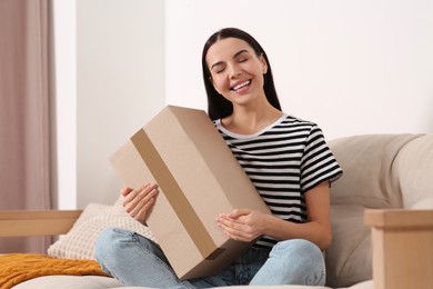 Photo of Happy young woman with parcel on sofa at home. Internet shopping