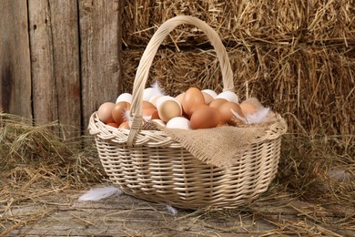 Photo of Wicker basket with fresh chicken eggs and dried straw in henhouse