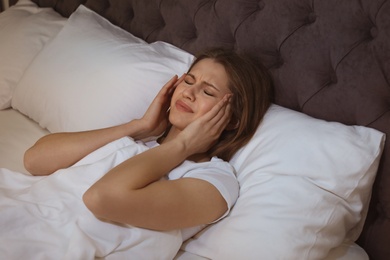 Photo of Young woman with terrible headache lying in bed at night