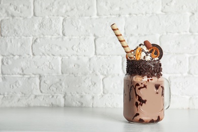 Photo of Mason jar of tasty milk shake with sweets on table near brick wall. Space for text