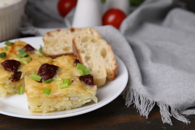 Photo of Tasty sausage casserole with green onion and bread on wooden table, closeup