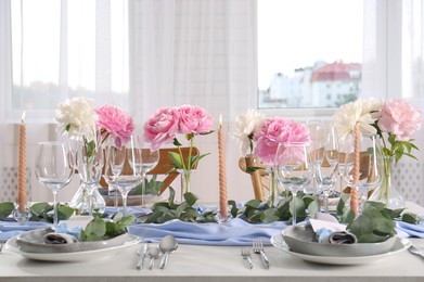 Photo of Beautiful table setting. Plates with greeting cards, napkins and branches near glasses, peonies, burning candles and cutlery on table in room