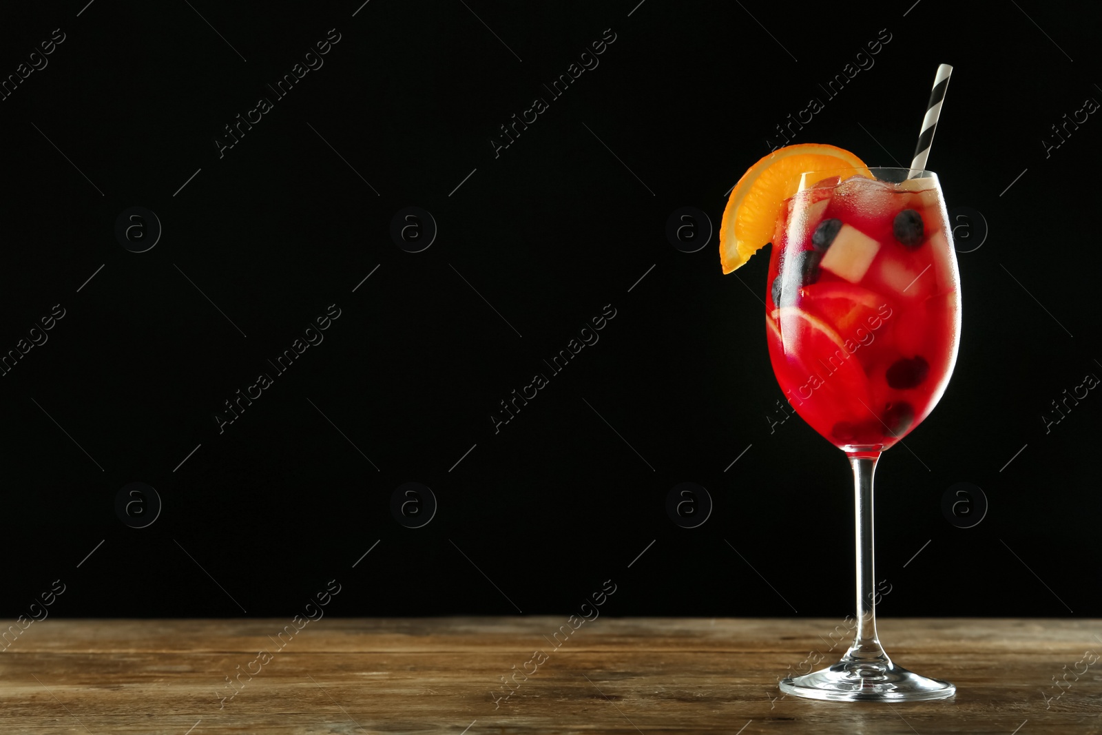 Photo of Glass of Red Sangria on wooden table against black background. Space for text