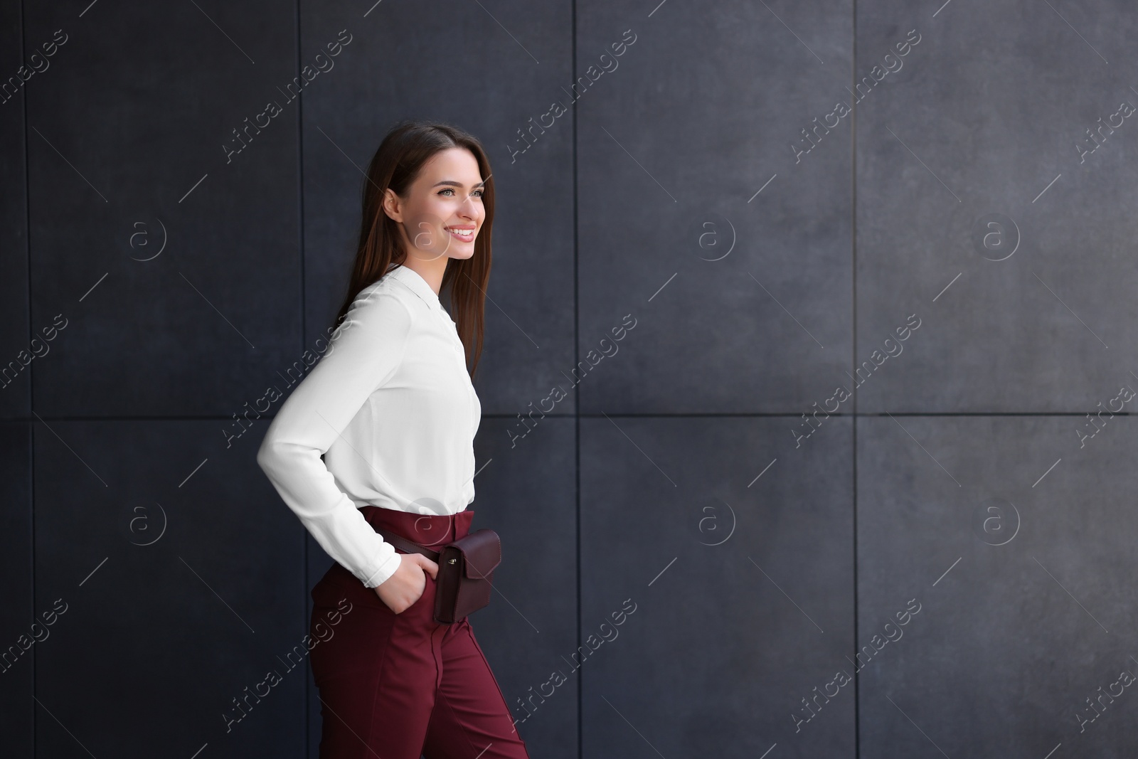 Photo of Young woman in formal clothes walking near grey wall outdoors, space for text