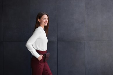 Photo of Young woman in formal clothes walking near grey wall outdoors, space for text
