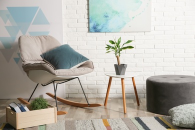 Photo of Comfortable rocking chair near brick wall in modern room interior