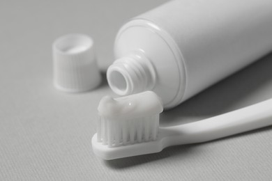 Plastic toothbrush with paste and tube on grey background, closeup