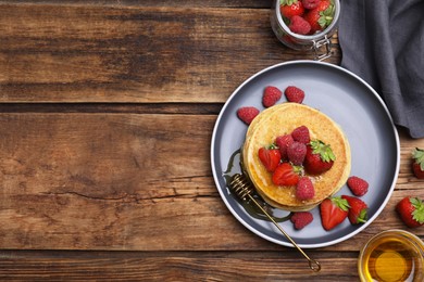 Tasty pancakes served with fresh berries and honey on wooden table, flat lay. Space for text