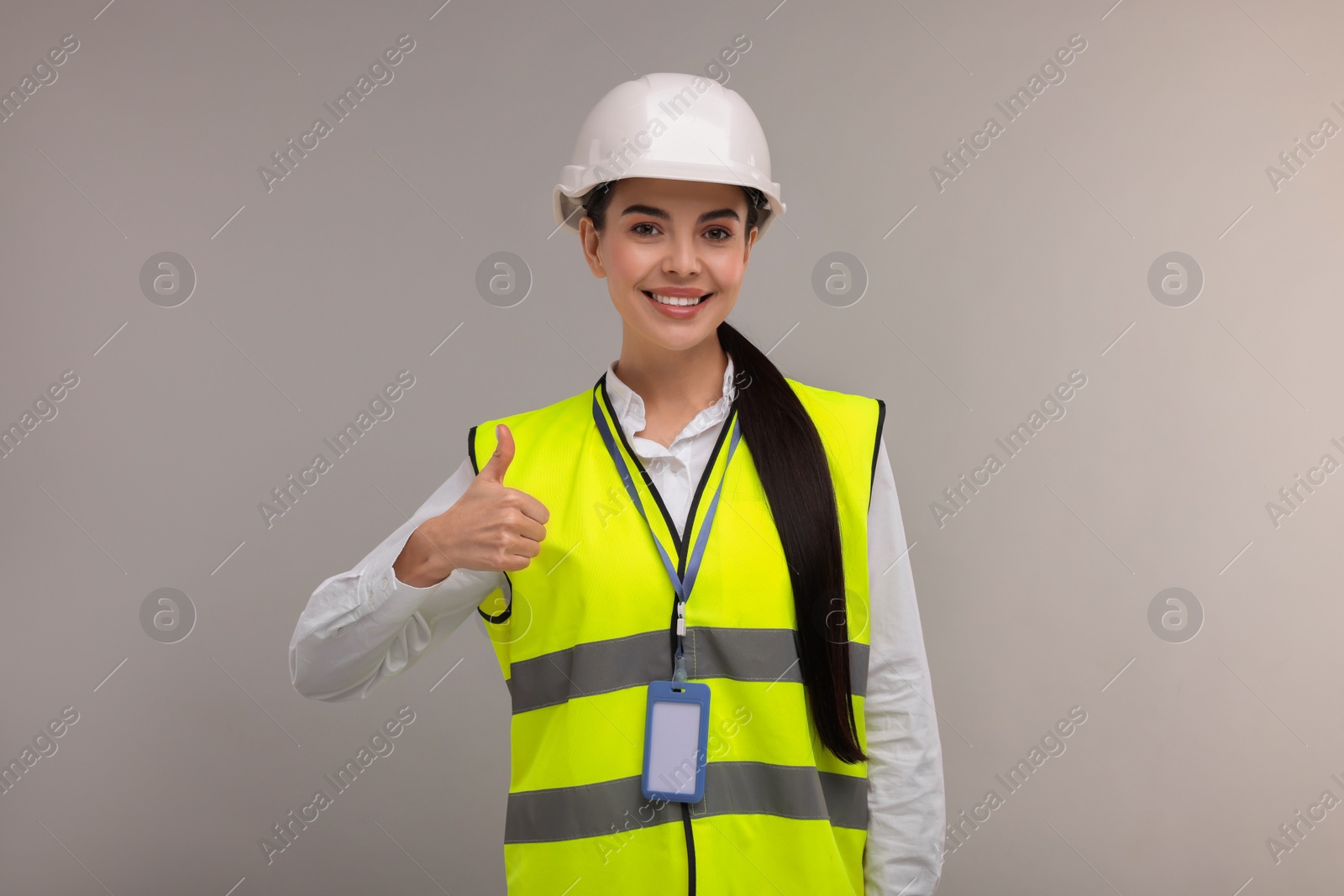 Photo of Engineer with hard hat and badge showing thumb up on grey background