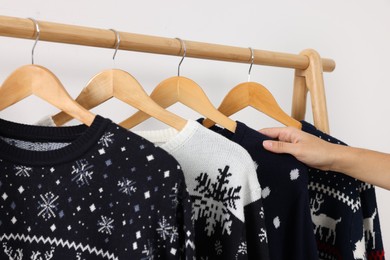 Woman choosing Christmas sweater from rack near white wall, closeup