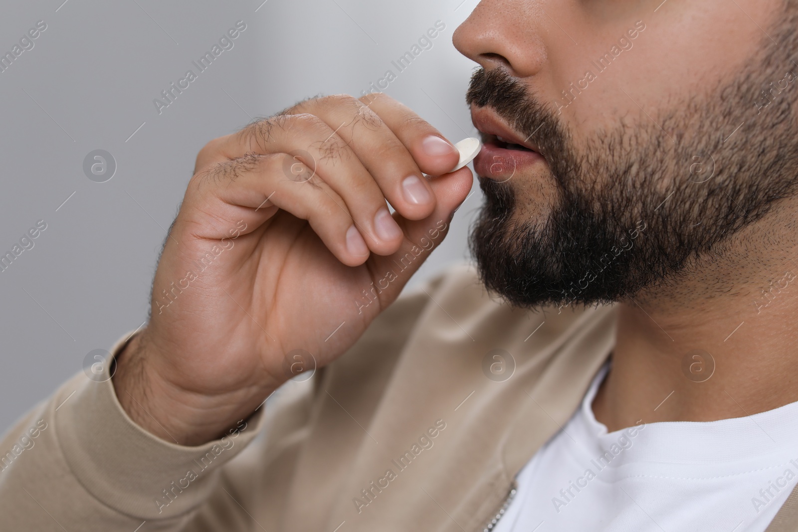 Photo of Man taking antidepressant pill on light grey background, closeup