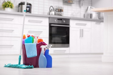 Photo of Bucket with cleaning supplies on floor in kitchen. Space for text