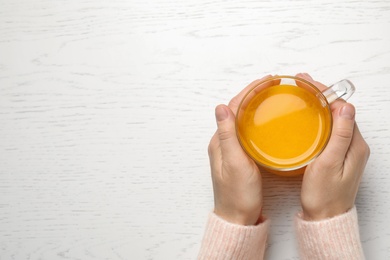 Woman with cup of fresh sea buckthorn tea at white wooden table, top view. Space for text