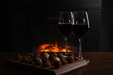 Photo of Red wine and chocolate truffles on wooden table against fireplace
