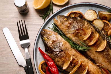 Photo of Tasty homemade roasted perches served on wooden table, flat lay. River fish