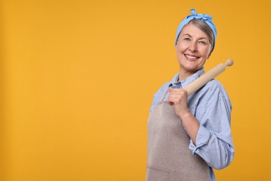 Happy housewife with rolling pin on orange background, space for text