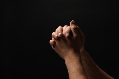 Religion. Christian man praying on black background, closeup. Space for text