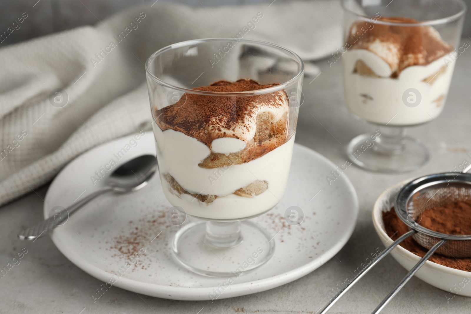 Photo of Delicious tiramisu in glass and sieve with cocoa powder on light table