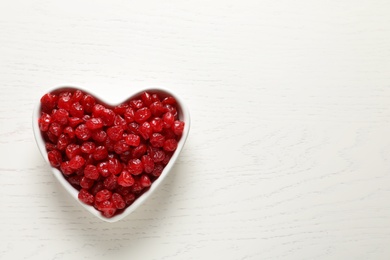 Photo of Heart shaped bowl of sweet cherries on wooden background, top view with space for text. Dried fruit as healthy snack