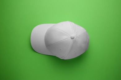 Photo of Stylish white baseball cap on light green background, top view