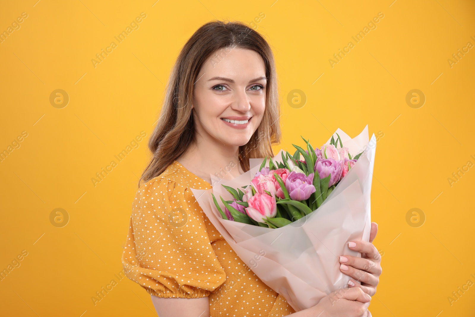 Photo of Happy young woman with bouquet of beautiful tulips on yellow background
