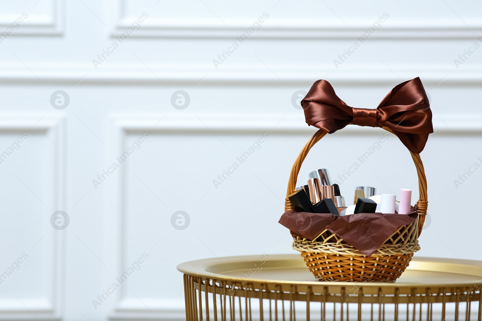 Photo of Gift set in wicker basket on golden table near white wall. Space for text