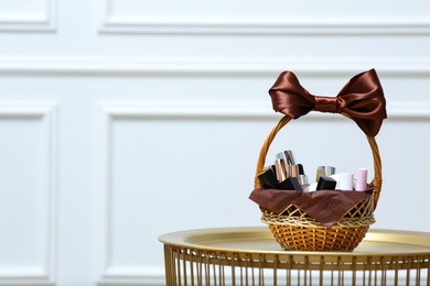 Photo of Gift set in wicker basket on golden table near white wall. Space for text