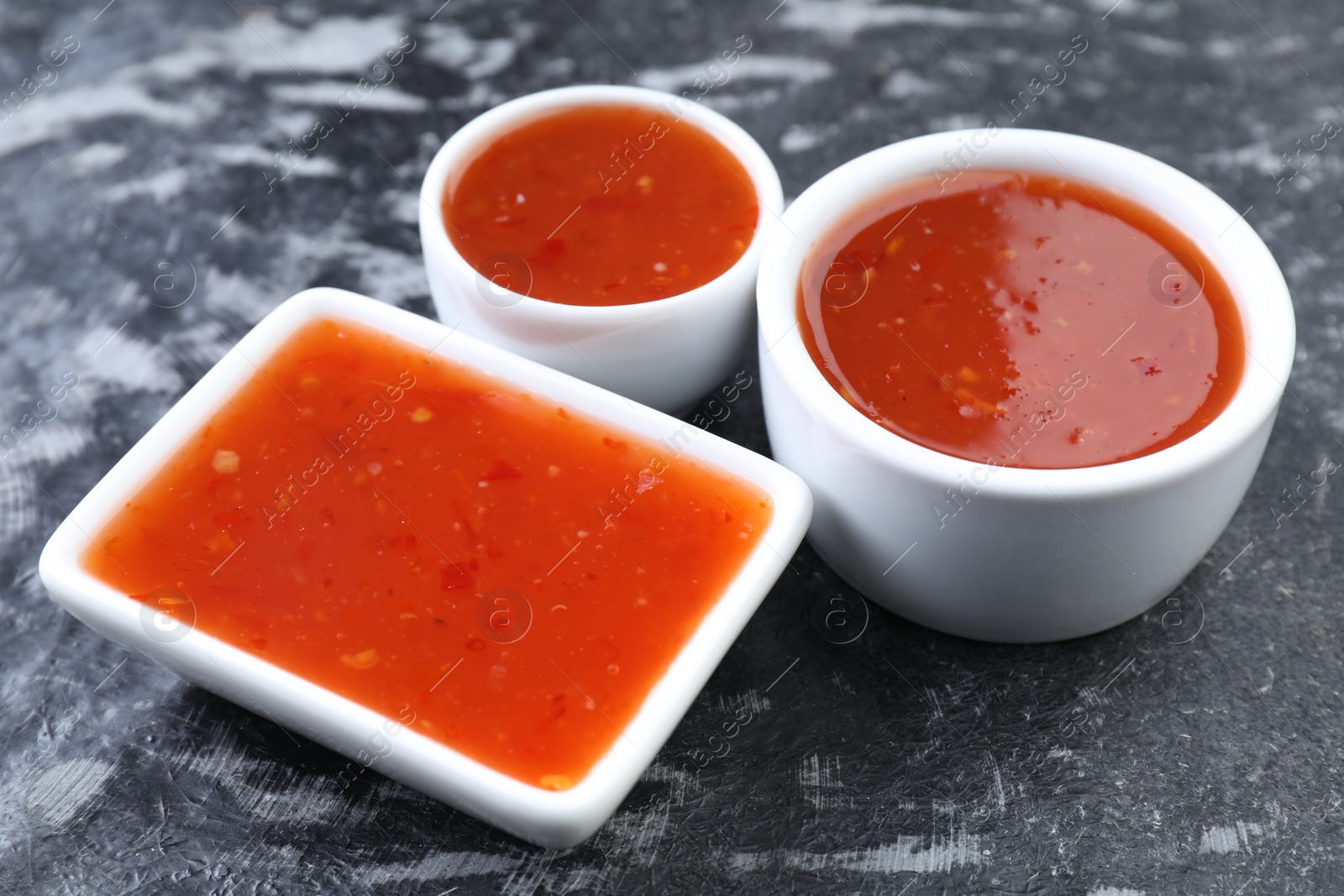 Photo of Spicy chili sauce on black textured table, closeup