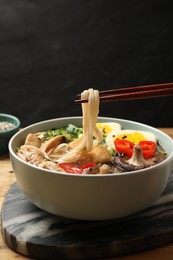 Photo of Eating delicious ramen with chopsticks on table, closeup. Noodle soup