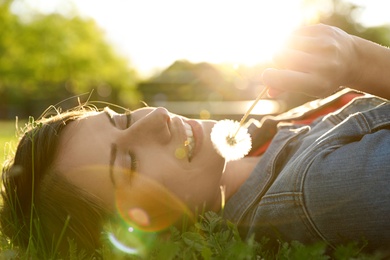 Photo of Young woman with dandelion in park on sunny day. Allergy free concept