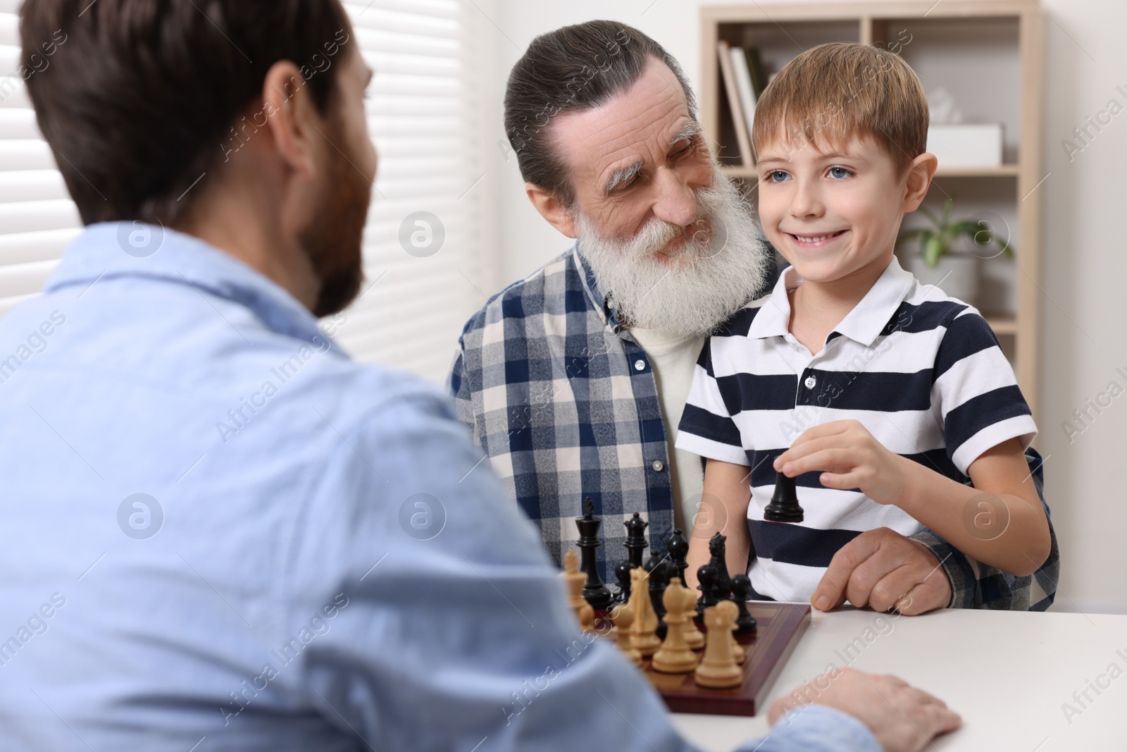 Photo of Family playing chess together at table in room