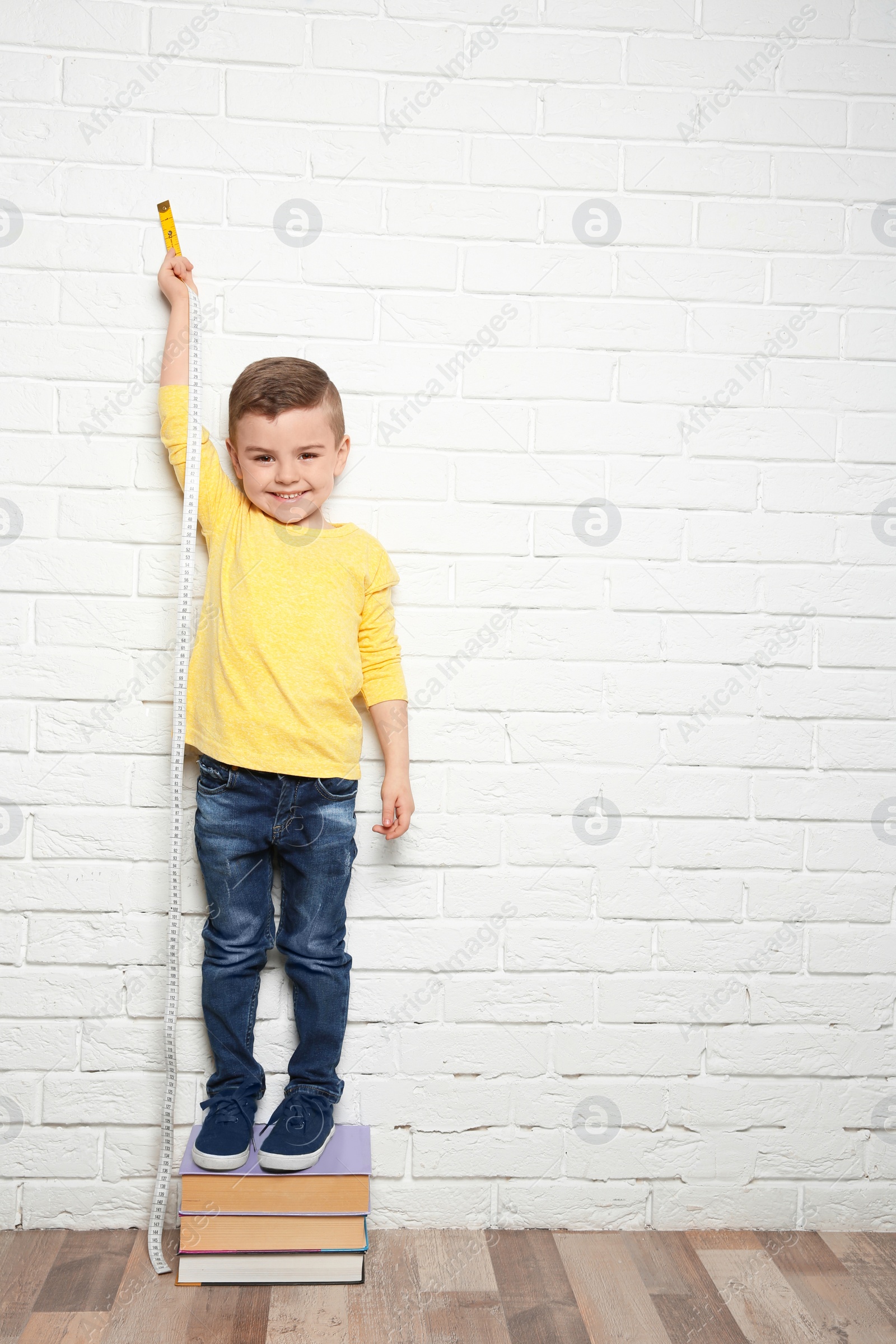 Photo of Little boy measuring his height near brick wall