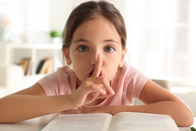 Photo of Little girl doing homework at table indoors